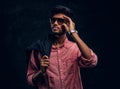 Vogue, fashion, style. Handsome young Indian guy wearing a pink shirt and sunglasses holding a jacket on his shoulder Royalty Free Stock Photo