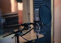 Voice microphone with shock mount and pop filter on professional tripod in audio recording studio.