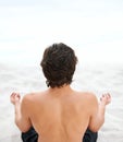 The voice of the sea speaks to his soul. Young handsome man sitting on the beach meditating. Royalty Free Stock Photo