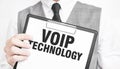 VOIP TECHNOLOGY inscription on a notebook in the hands of a businessman on a gray background, a man points with a finger to the