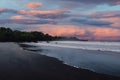 Volcanic beach with ocean waves in Bali. Black sand coastline and sunset or sunrise cloudy sky