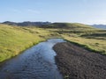 Volcanic hills, lush grass and blue river next to camping site on Alftavatn lake. Summer sunny day, landscape of the