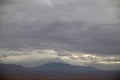 Volcano with snow on the peak under a dramatic sky and sunbeams sneaking through the clouds. San Pedro de Atacama,