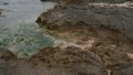 Volcanogenic rock slab filled with tide water on the seashore. Volcanic rocks on the edge of clear sea water. Natural rocky