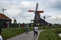 Bicyclists ride down a path past traditional windmills on a cloudy day at Volendam, located on the Markermeer Lake, northeast of