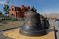 New bells of different sizes stand on a wooden platform against the background of the Nevsky Cathedral under construction in Volgo