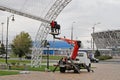 Workers in a bucket of a truck crane install LED lighting on an arch in Victory Park