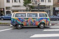 a Volkswagen Bus covered in colorful paintings driving on the street surrounded by cars and apartments in San Francisco California