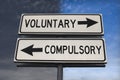 Voluntary versus compulsory road sign with two arrows on blue and grey sky background. White two street sign with arrows on metal Royalty Free Stock Photo