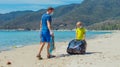 Volunteer blue face mask lazur sea sand beach. Son helps father hold black bag for pick up garbage. Problem spilled