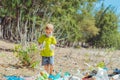 Volunteer boy in face mask helps to pick up garbage which pollute beach near forest. Problem of spilled rubbish trash