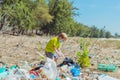 Volunteer boy in face mask helps to pick up garbage which pollute beach near forest. Problem of spilled rubbish trash