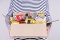 Volunteer hands holding food donations box with grocery products on white desk