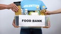 Volunteer holding food bank container, hands putting provision in box, help