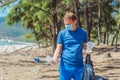 Volunteer man in face mask pick up garbage pollute beach near sea, hold look at discarded disposable plastic cups