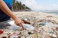 Volunteer tourist hand is clean up garbage and plastic debris on dirty beach by collecting them into big blue bag