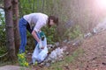 Volunteer woman picking trash on forest near lake in park, collecting garbage.