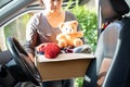 Volunteer woman provide clothing donation box with used clothes and doll in car to support help for refugee, homeless or poor