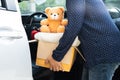 Volunteer woman provide clothing donation box with used clothes and doll in car to support help for refugee, homeless or poor