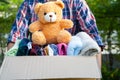 Volunteer woman provide clothing donation box with used clothes and doll to support help for refugee, homeless or poor people in