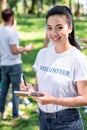 volunteer writing in textbook while friends cleaning park