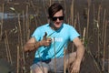 A volunteer young man in blue t-shirt giving  thumb up during planting sapling tree in deep mud at mangrove forest for increasing Royalty Free Stock Photo