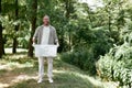 Volunteering concept. Young happy man eco activist collecting plastic in the forest or park, holding recycle bin and