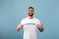 Volunteering job concept. Portrait of happy arab male activist showing his t-shirt with volunteer print inscription