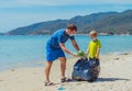 Volunteers blue face mask paradise beach sand lazur sea. Father son pick up garbage into black bag. Problem spilled