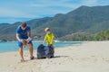 Volunteers blue face mask paradise beach sand lazur sea. Father son pick up garbage into black bag. Problem spilled