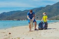 Volunteers blue face mask paradise beach sand lazur sea. Father son pick up garbage into black bag. Problem spilled