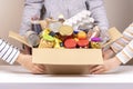 Volunteers hands holding food donations box with grocery products on white desk