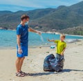 Volunteers paradise beach sand lazur sea. Man, boy pick up garbage into black bag. Son refuse to wear blue face mask