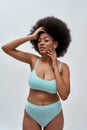 Voluptuous young mixed race female model with afro hair wearing blue underwear posing for camera, standing isolated over