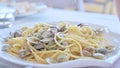 Vongole pasta is white. A traditional Italian dish with small seashells and spaghetti. A man winds food on a fork in a