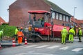 Paver laying asphalt on a new road with workers helping