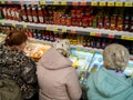 Elderly women choose products in the refrigerators of the store