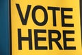 vote here capital letters in black on yellow background against blue background Royalty Free Stock Photo