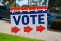 A VOTE Sign At A Polling Place On Green Grass Near A Parking Lot