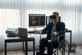 VR at work. Young male web developer in a wheelchair wearing virtual reality glasses while working at his workplace in Royalty Free Stock Photo