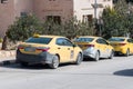 Yellow taxi cars stand parked on a street side in Wadi Musa next to entrance to Petra