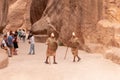 Two Bedouins dressed in the uniform of Nabatean warriors stand for tourists in front of the entrance to the gorge Al Siq in Petra