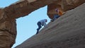 Tourists perilously climb a steep rock face to reach scenic natural rock bridge