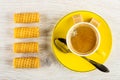 Wafer rolls, yellow cup with coffee, spoon, sugar on saucer on table. Top view