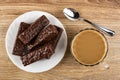 Wafers in chocolate in white plate, cup of coffee with milk, spoon on wooden table. Top view Royalty Free Stock Photo