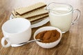 Wafers with porous chocolate in white plate, cup, pitcher with milk, spoon in cocoa with sugar in bowl on wooden table Royalty Free Stock Photo