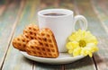 Waffle biscuits in shape of heart with cup of coffee and flower on rustic background for Valentines day