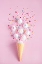 waffle cone and white twisted meringue with confectionary decorations on pink background.