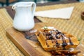 Waffles with chocolate icing sugar and syrup on a wooden plate