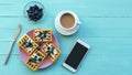 Waffles with cream cheese and blueberries on a pink plate, coffee cup and phone on turquoise wooden table. Top view, flat lay Royalty Free Stock Photo